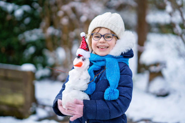 милая маленькая дошкольница в очках делает мини-снеговика. очаровательный здоровый счастливый ребенок играет и веселится со снегом, на све - playground snow winter little girls стоковые фото и изображения