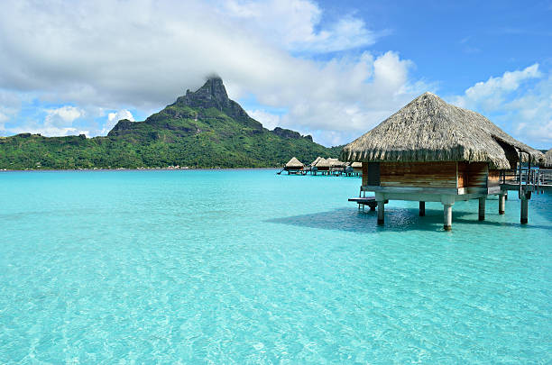 Luxury overwater vacation resort on Bora Bora island Luxury overwater thatched roof honeymoon bungalow in a vacation resort in the clear blue lagoon with a view on Mt. Otemanu and the tropical island of Bora Bora, near Tahiti, in pacific French Polynesia. bora bora mountain stock pictures, royalty-free photos & images