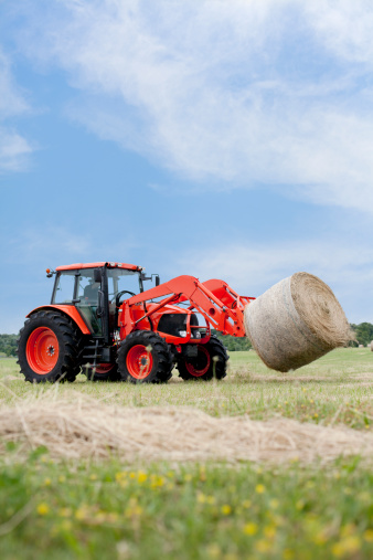 Tractor hauling a round bale an open field with blue sky.