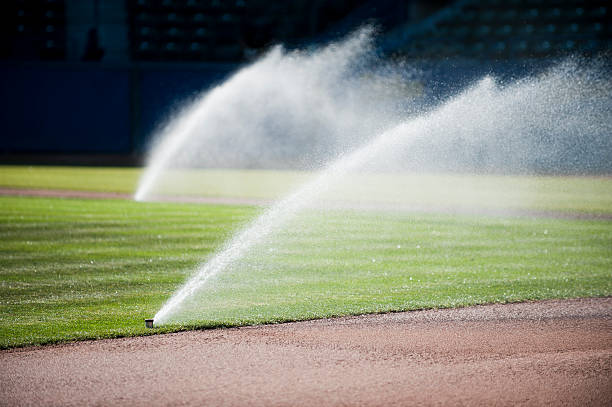 Two sprinklers watering a baseball field.