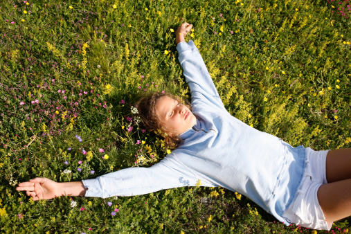 Young girl with closed eyes lying in a satisfaction mood on a field of flowers