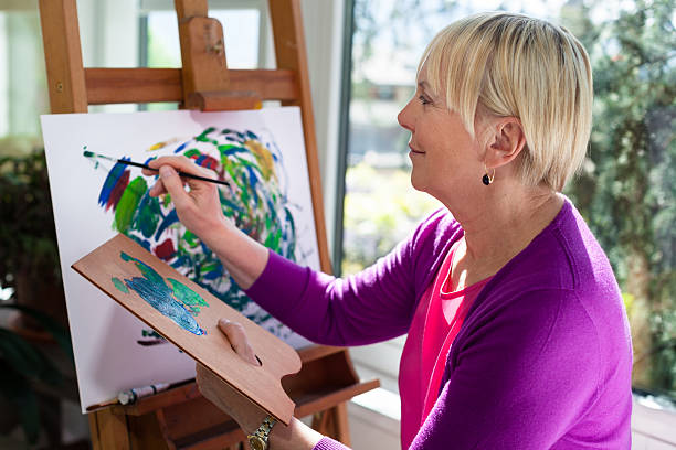 счастливый пожилые женщина, живопись для развлечения в домашних условиях - easel adult art creativity стоковые фото и изображения