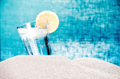 A drink with ice and lemon on the beach in the summer on blue background