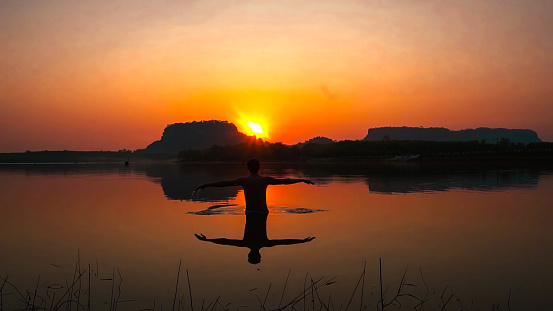 A man Doing Yoga  in river at Sunset.