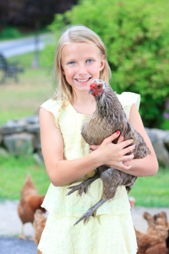 Young Blonde Girl in the Garden with Chickens in a Yellow Dress