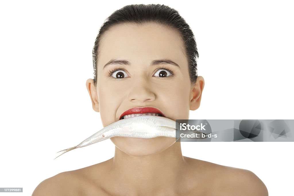 Woman holding fresh fish in her mouth Young woman holding fresh fish in her mouth. Concept of healthy eating of fishes with omega 3. Eating Stock Photo