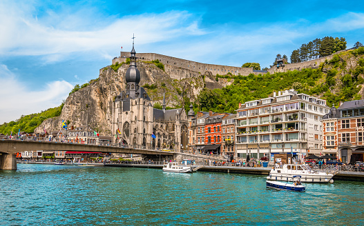 Panoramic view of the city of Dinant with collegiate church, old buildings and bridge over the Meuse on a beautiful summer day. City view from boat trip on Meuse river. Colorful travel image of Dinant Belgium.