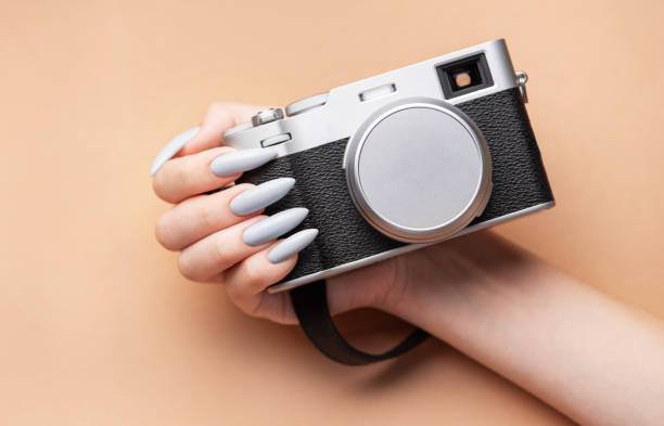 istock Woman's hand with grey nail polish holding camera 1774031413