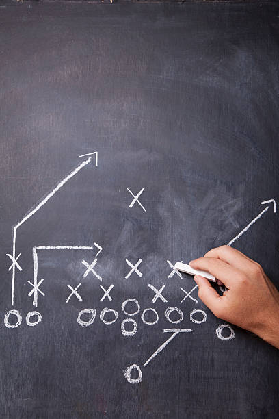 Football Coach Draws Play A hand draws a football play on a chalkboard with chalk leaving room for copy. american football game plan stock pictures, royalty-free photos & images
