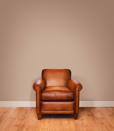 Leather armchair on a wooden floor against a plain background wall with lots of copyspace. The wall has a clipping path.