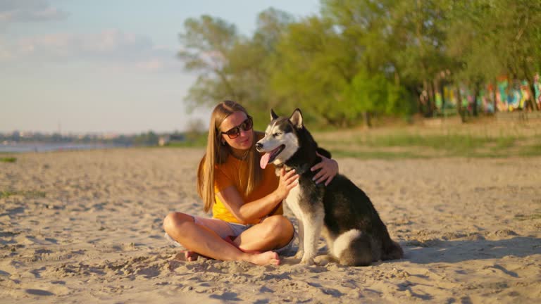 Happy pet owner relaxing and hugging her dog on the beach in summer. Woman enjoying walk with her pet dog