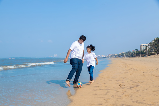 Happy indian Father and daughter enjoying summer vacation, Playing football on beach.