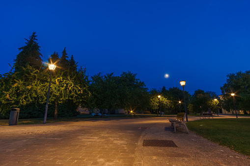 Empty park bench in citadel at night during blue hour with moon on the sky in Pamplona, Navarra, Spain
