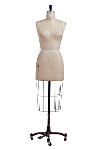 Antique dressmakers mannequin torso form with beige linen fabric cover and black wrought iron stand on castors. Front view, vertical, isolated on white, copy space.