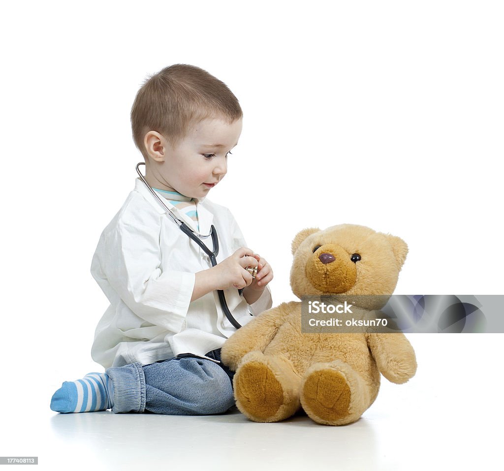 Adorable child with clothes of doctor examining teddy bear Adorable boy with clothes of doctor on white background Child Stock Photo