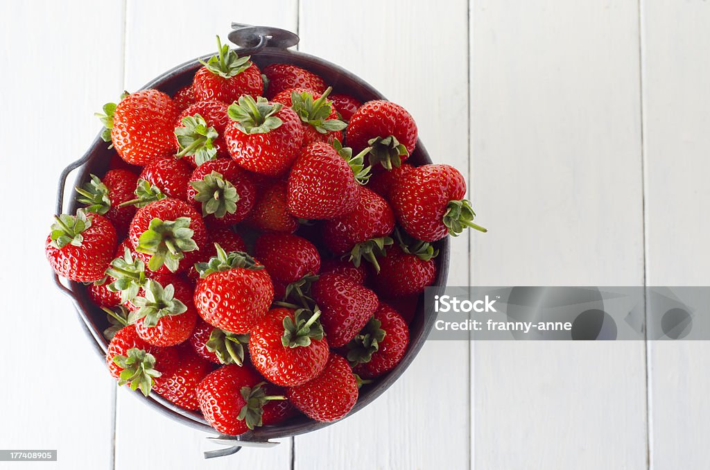 Strawberry Harvest "Overhead shot of a tin pail filled to the top with fresh strawberries, on a wooden planked table, painted white.  Copy space to right of frame." Abundance Stock Photo