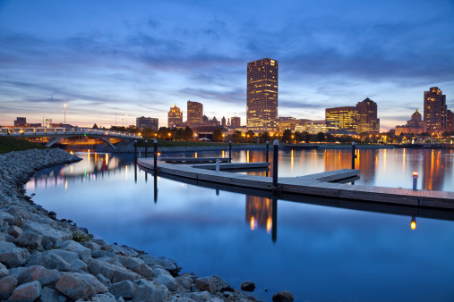Image of Milwaukee skyline at twilight with city reflection in lake Michigan and harbor pier.