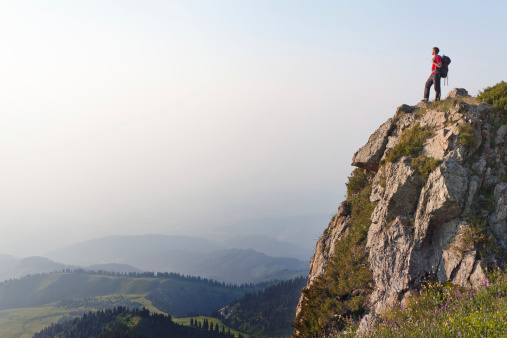 Image of mountain scenery, on top of which stands the silhouette of a tourist, who looking into the valley.