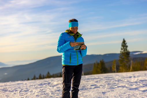 Woman hiker in warm clothing using mobile phone on snowy mountain landscape