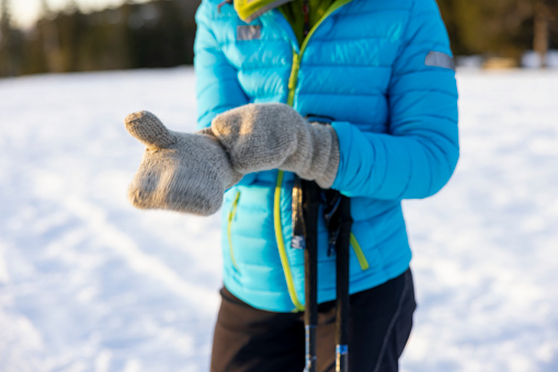 Midsection of woman skier putting on her hand gloves while getting ready for skiing on snowy winter landscape