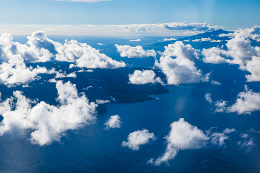 Flying in the blue sky with fluffy white clouds above the pacific ocean near Hawaii.