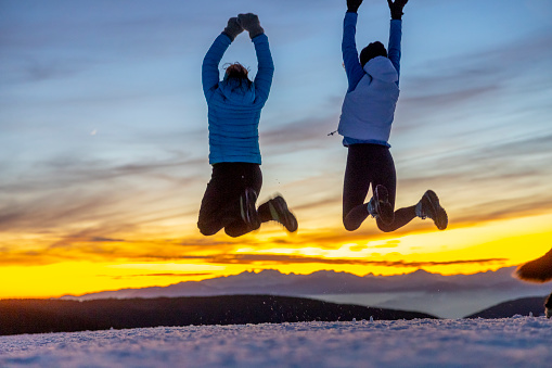 Rear view of two carefree women friends in warm clothing jumping in winter nature