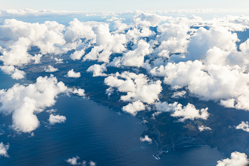 Flying in the blue sky with fluffy white clouds above the pacific ocean near Hawaii.