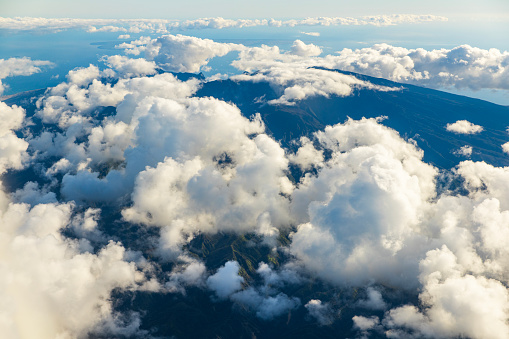 Flying in the blue sky with fluffy white clouds above the mountains of Hawaii.
