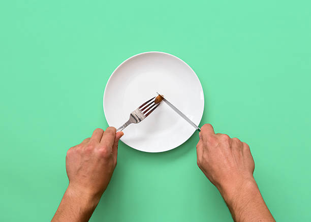Knife and fork cutting into small diet meal on white plate small diet meal serving size stock pictures, royalty-free photos & images