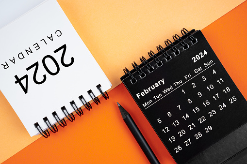 February 2024 desk calendar black and white color with pencil on orange color background.