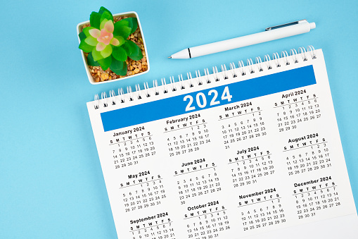 Hello 2024 calendar. 12 months desk calendar 2024 with pen on blue background.