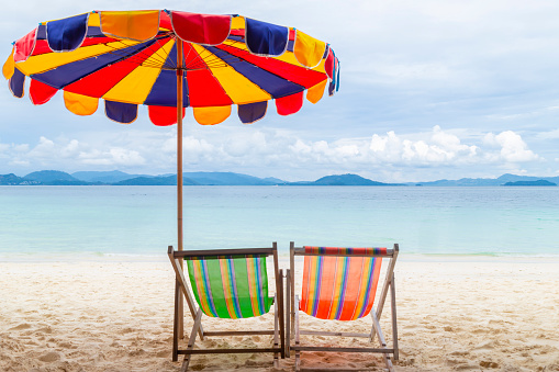Subject: Horizontal view of two orange beach chairs under a tan striped umbrella, alone on a quiet, clean, sunny beach on the Pacific coast.