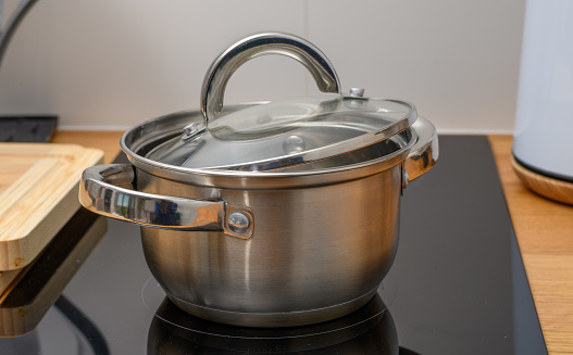 A hotpot kettle with boiling water is placed on the electric stove on the dining table. Close-up at the glass lid. Food utensil object photo. close-up and selective focus.