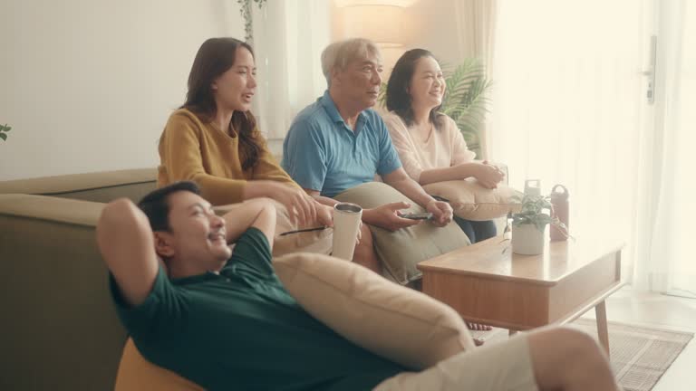 Quality Family Moments: Happy Asian Parents and Teenage Girl Enjoying TV Together in Cozy Living Room.