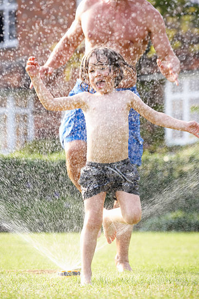 istock Father And Son Running Through Garden Sprinkler 177412913