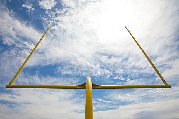 Yellow american footbal uprights against a partially cloudy sky. Viewed from below and the back of the field goal.