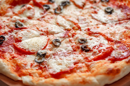 Pizza with cheese and salami and black olives, close-up, selective focus