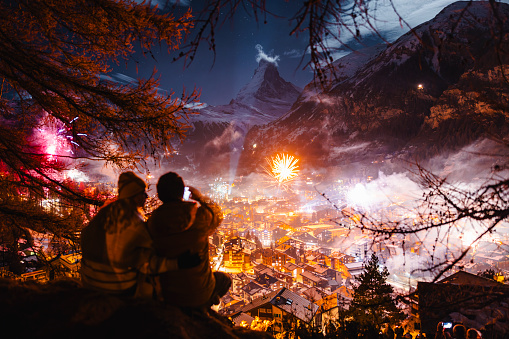 A couple sits, admires and talking pictures of fireworks at celebration of New Year at Zermatt and Matterhorn peak