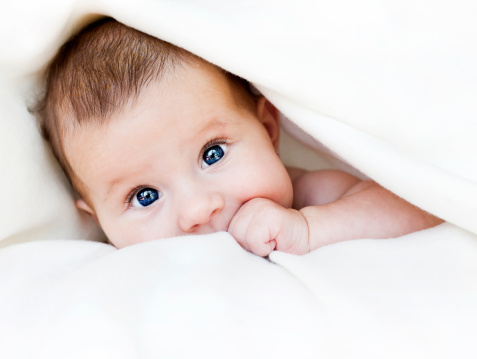 Joyful little baby boy smiling and laying on front on bed.