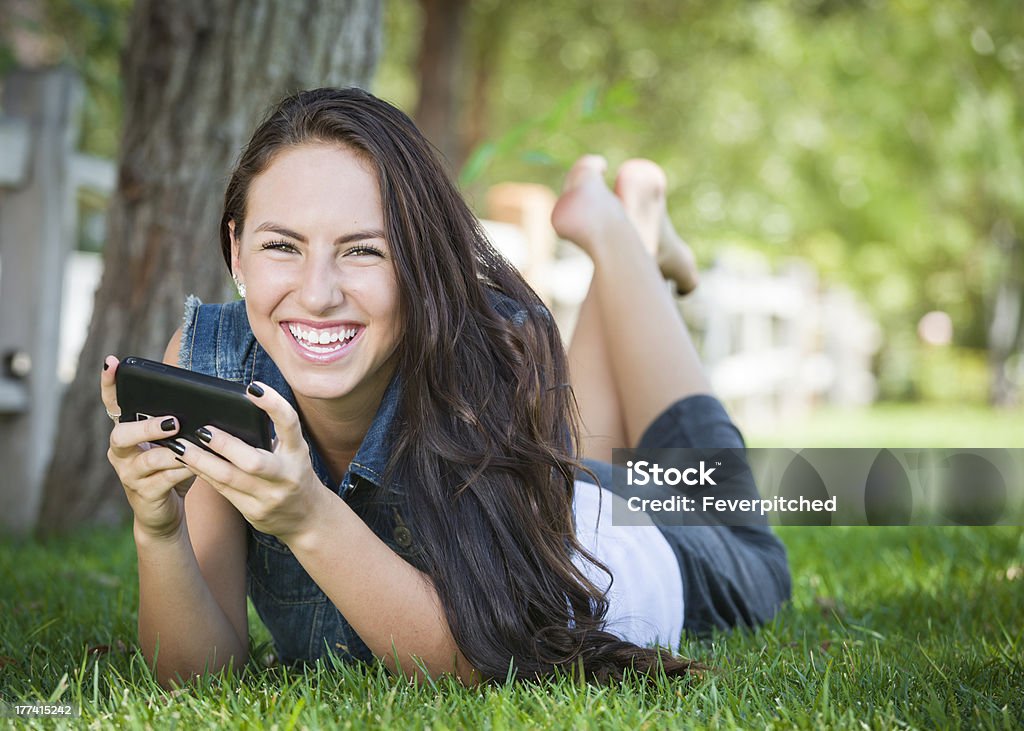 Mixed Race Young Female Texting on Cell Phone Outside Attractive Happy Mixed Race Young Female Texting on Her Cell Phone Outside Laying in the Grass. Adult Stock Photo