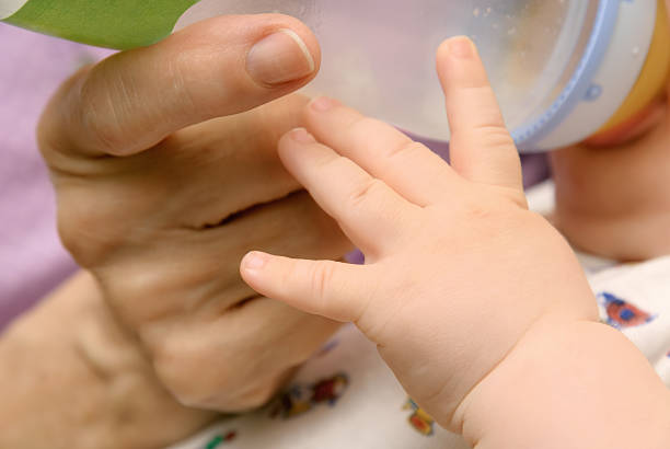 Closeup of baby's and grandmother's hands while the infant drinks from a bottle