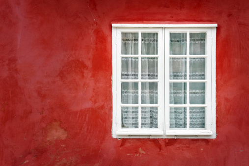 Decorative white window on an old red stucco wall