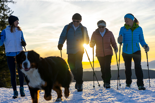 Old parents and two mature daughters with Bernese mountain pet dog hiking on snowy winter landscape