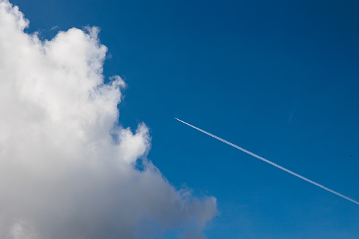close up view, looking directly up, of an airplane flying in the blue sky, partially covered by a white cloud. natural scene illuminated by the sunlight