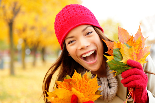 Excited happy fall xwoman smiling joyful and blissful holding autumn leaves outside in colorful fall forest. Beautiful energetic mixed race Caucasian / Asian Chinese young woman.