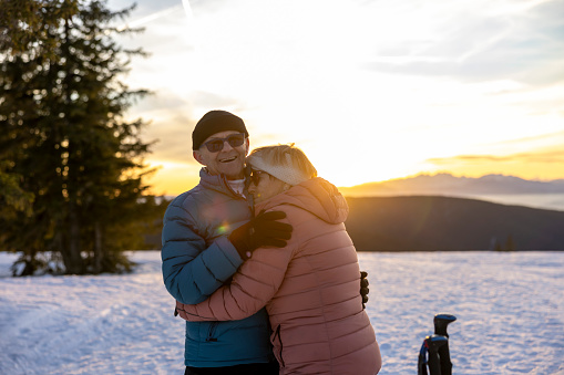 Senior couple in warm clothing embracing each other on snowy winter landscape