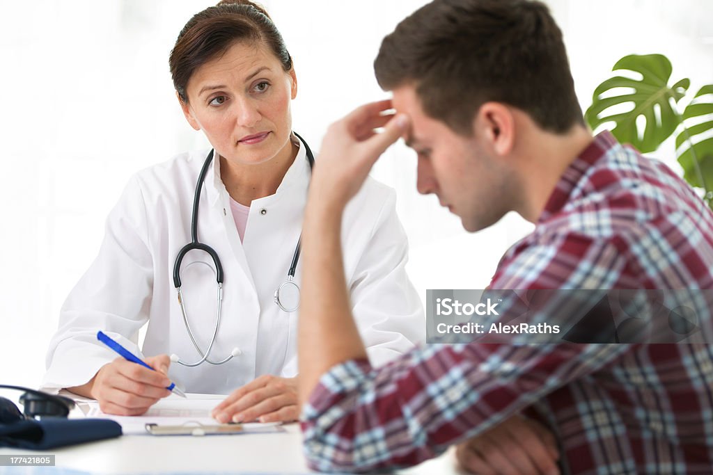 Female doctor with male patient who is holding his head doctor talking to her male patient at office Doctor Stock Photo