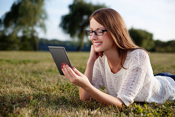 jeune femme lisant un e-book dans la nature - women grass glasses e reader photos et images de collection