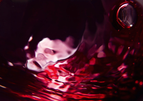 Red wine poured into a wine glass on black floor front of white background.