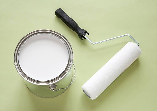 Can of white paint and roller on green background stock photo